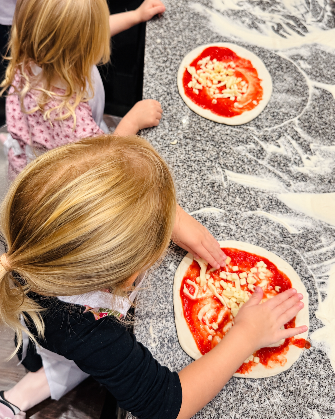 Kinder belegen ihre eigenen Pizzen mit Tomatensauce und Käse